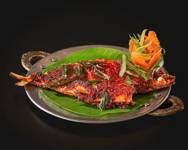 Spicy whole fried fish topped with curry leaves on a banana leaf and metal platter.