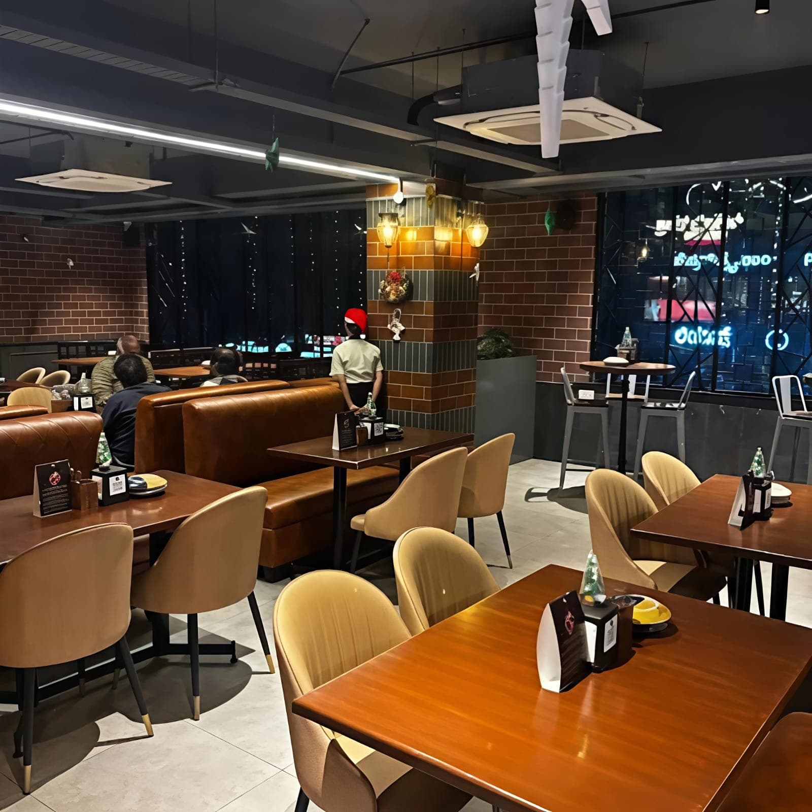 Modern restaurant interior with wooden tables, tan chairs, and leather booths overlooking city lights.