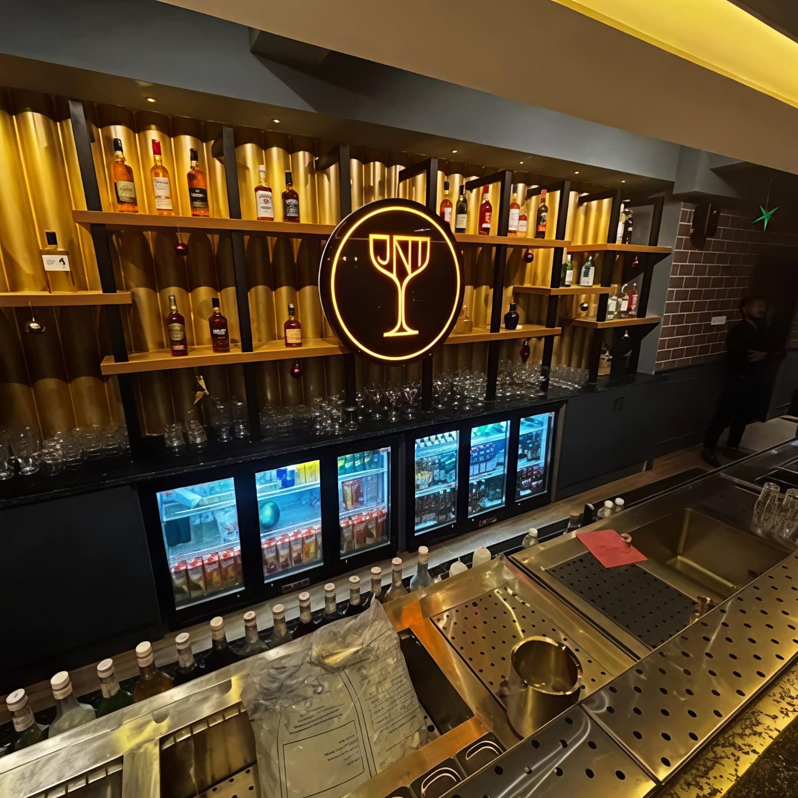 Modern bar with gold fluted walls, liquor shelves, and a glowing circular cocktail glass logo.