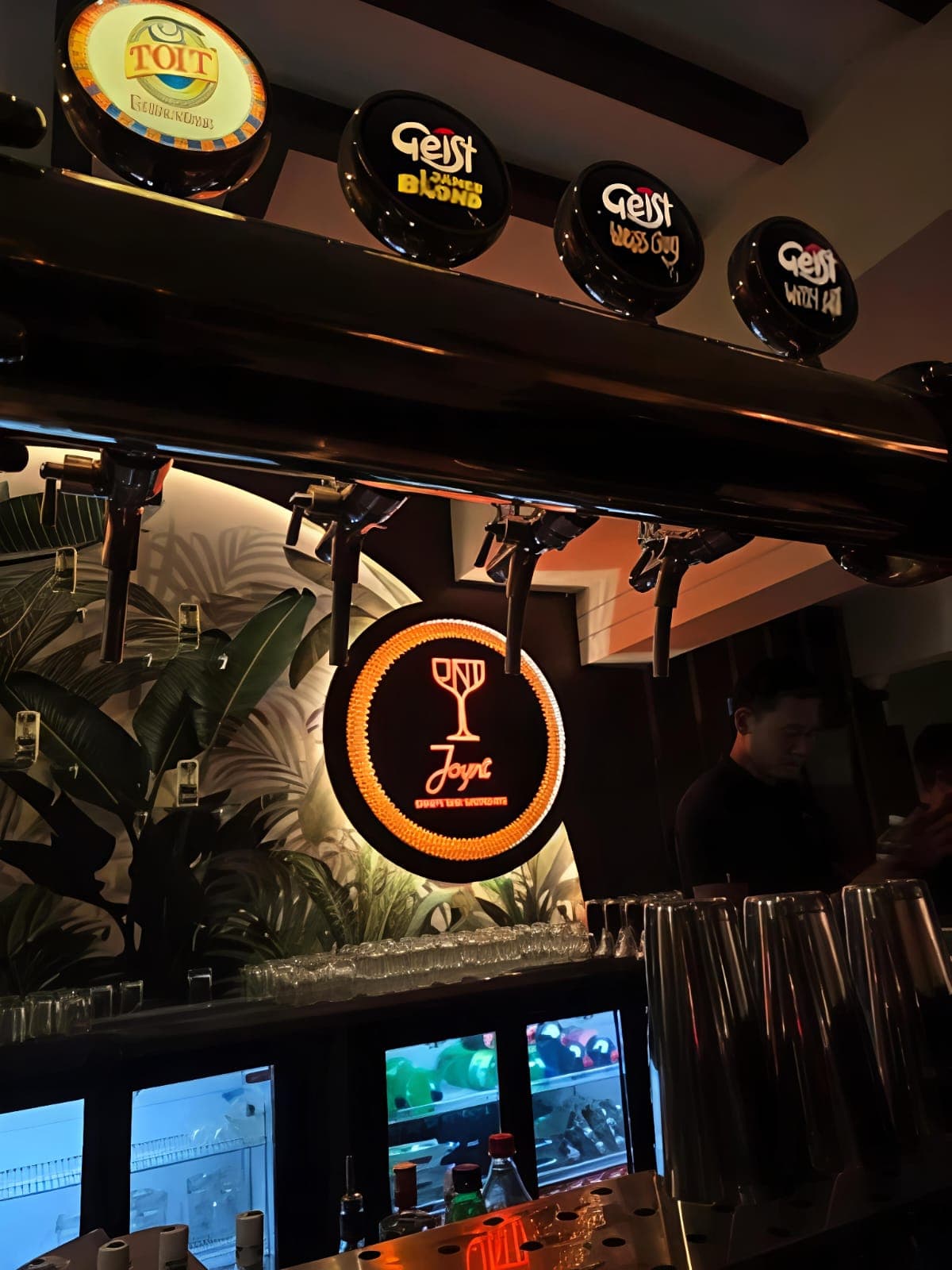 Dimly lit bar with beer taps, a glowing sign, and a bartender behind the counter.