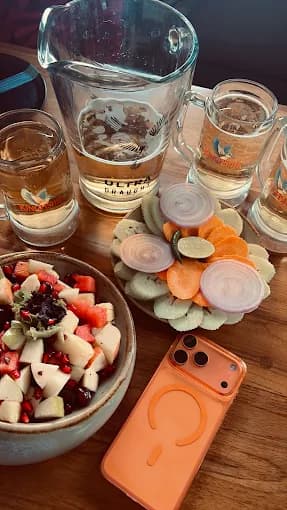 Beer pitcher and mugs with fruit salad, sliced vegetables, and an orange smartphone.