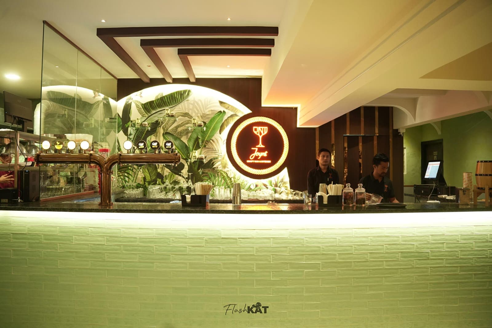 Modern bar with two staff, tropical leaf mural, and a circular glowing neon sign.